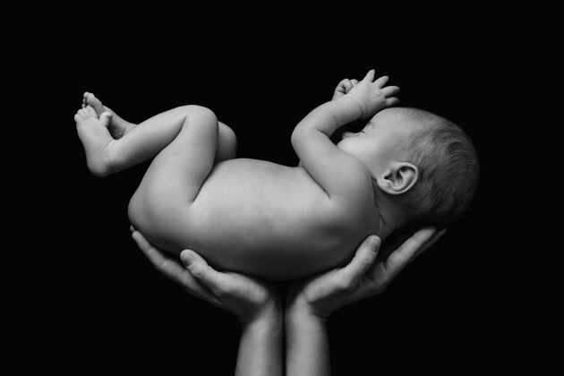 保护可爱的新生婴儿在妈妈的手上贴着黑墙身体小分娩