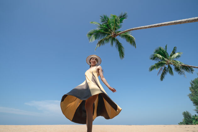 放松走在椰子树下的女人 在沙滩上 天空湛蓝沙滩自由连衣裙