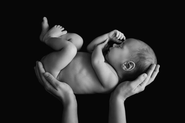 婴儿可爱的新生婴儿在妈妈的手上贴着黑墙出生单色可爱