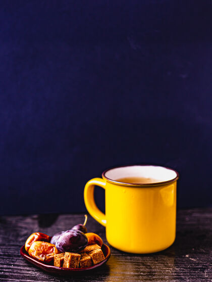杯子把黄色的茶杯放在木架上 深蓝色的背景 水果放在一个小瓷盘上假日杯子创意
