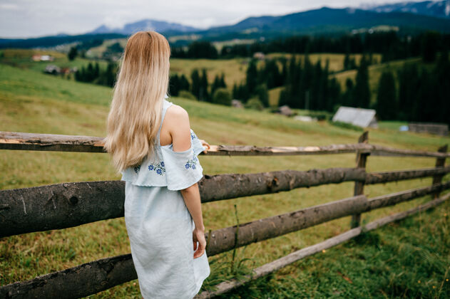 乡村年轻漂亮的金发碧眼的女孩穿着蓝色的裙子 在乡村的篱笆旁摆姿势木头金发女孩