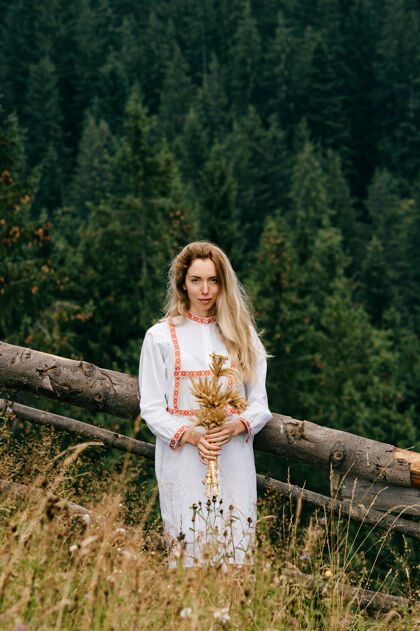 金发年轻迷人的金发女孩 身穿白色刺绣裙 在风景如画的草地上摆着小穗花束的姿势年轻自然女人