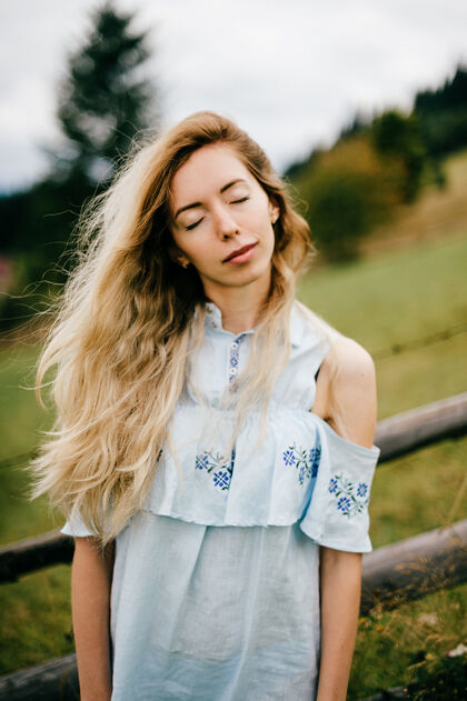 自然年轻漂亮的金发碧眼的女孩 穿着蓝色的裙子 在乡村的篱笆边摆姿势优雅乡村女孩