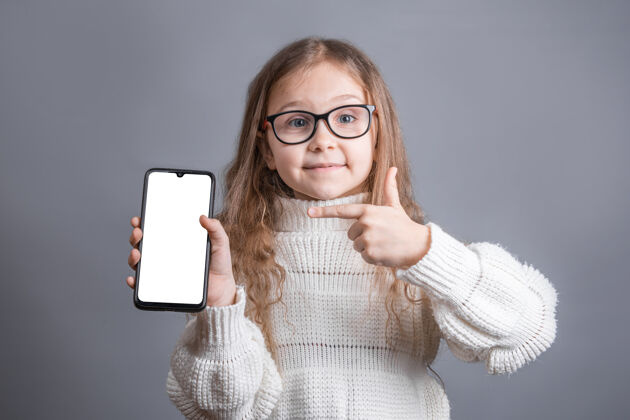 显示一个年轻漂亮的小女孩 金发飘逸 穿着白色毛衣 手持一部手机技术儿童成人