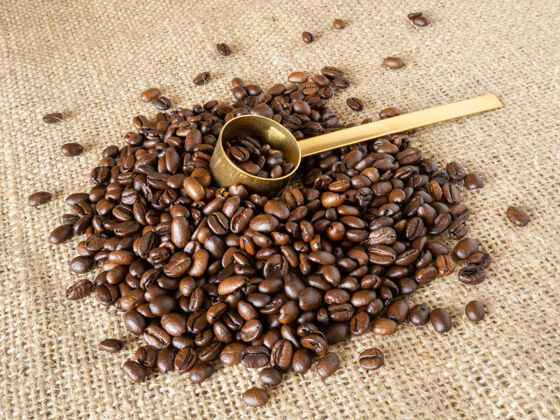 农作物咖啡豆与黄金测量匙亚麻质地的背景木头饮料浓缩咖啡