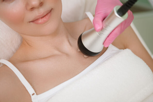 专业一个美容师使用射频升降装置对女性客户的胸部修剪镜头护理年龄面部