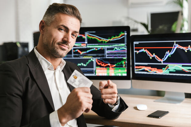肖像30多岁的欧洲商人穿着西装 坐在办公室里拿着信用卡 在电脑上处理数字图像数字信用财务