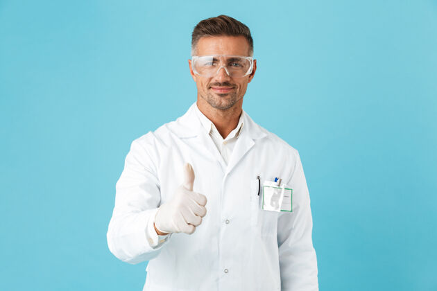 白种人自信的男医生穿着制服孤立地站在蓝色的墙上 竖起大拇指医生医学科学家