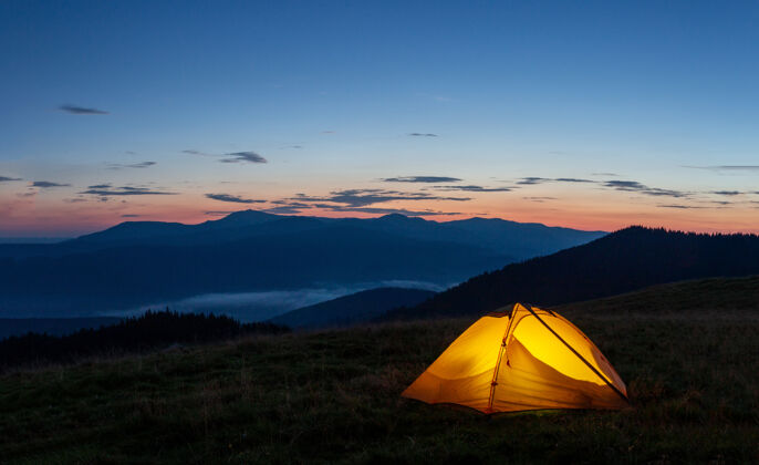 旅行傍晚或清晨 山上的橙色发光帐篷山旅行露营