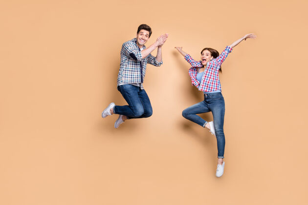 无忧无虑两个人的全身照片疯狂的女士家伙跳高享受夏季时间第一个周末穿休闲格子牛仔裤衣服孤立米色背景飞行旅游运动