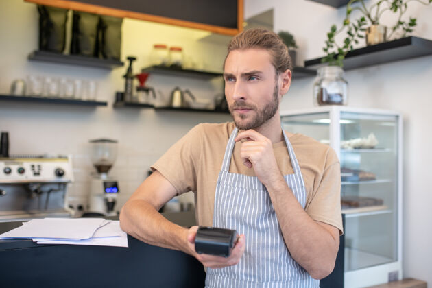 利润年轻人一个沉思的成年男子站在咖啡馆柜台旁 手里拿着一个小键盘考虑破产男人