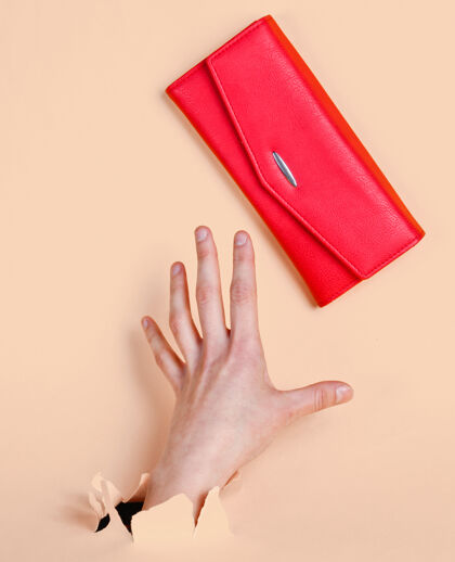 人女人的手通过撕破的黄色粉彩拿着红色的钱包纸简约创意时尚理念创意内红色钱包