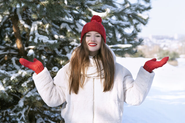 户外快乐美丽的黑发女孩戴着红帽子和布波在雪林阳光帽子乐趣