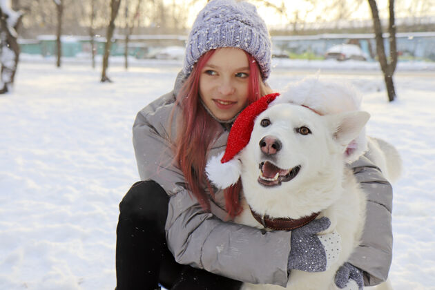 冬天这个女孩在冬天愉快地与大自然中戴着圣诞老人帽子的狗交流女孩雪友谊