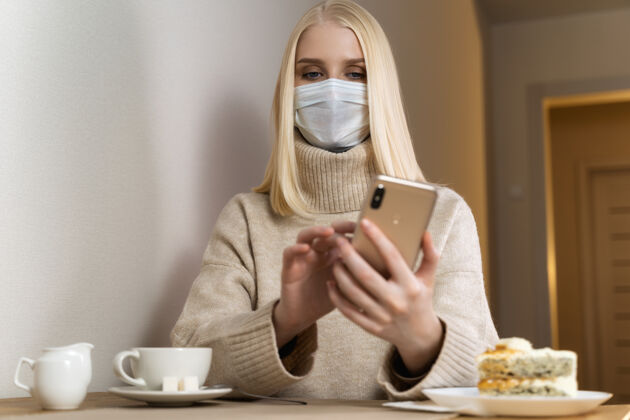 污染戴着防护面罩的严肃女人在咖啡馆里看智能手机看新闻手机医疗保健坐姿