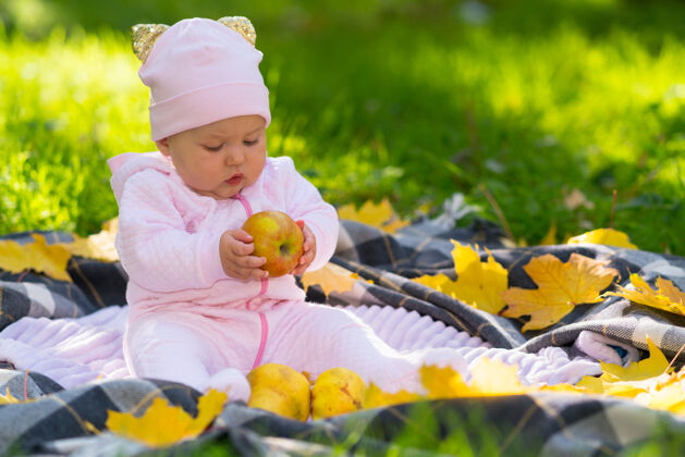 迷人小女婴抱着一个秋天的苹果 坐在花园草坪上的地毯上好奇地看着它享受年轻座位