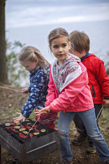 烧烤新的正常逃生步骤 野生自然步行和家庭户外娱乐孩子们当父母在火旁煮奶酪和香肠的时候玩得开心 周末徒步旅行 生活方式秋天旅游肮脏