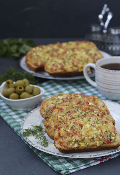 自制自制热三明治与奶酪和香肠在一个盘子里 橄榄和咖啡杯在格子桌布上 垂直格式 特写膳食早餐橄榄