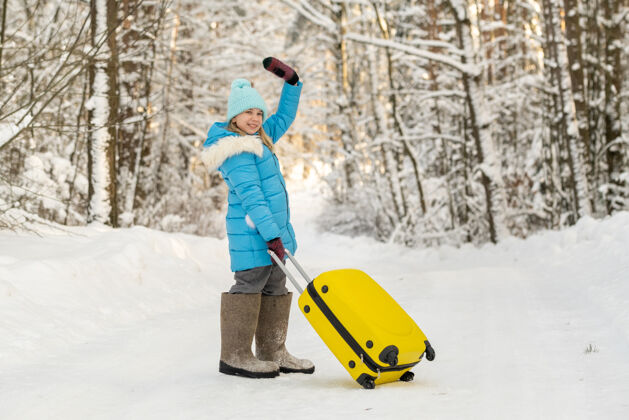 娱乐冬天 一个穿着毡靴的女孩在一个寒冷的雪天带着一个手提箱行李路下雪