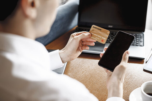 客户男人坐在桌子上用信用卡和智能手机的手控股借记钱