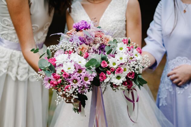 手身着优雅礼服的新娘和伴娘们站在那里 手拿着一束束淡粉色的鲜花和绿色的缎带自然年轻美丽的女孩在户外手持婚礼花束女性礼服国家