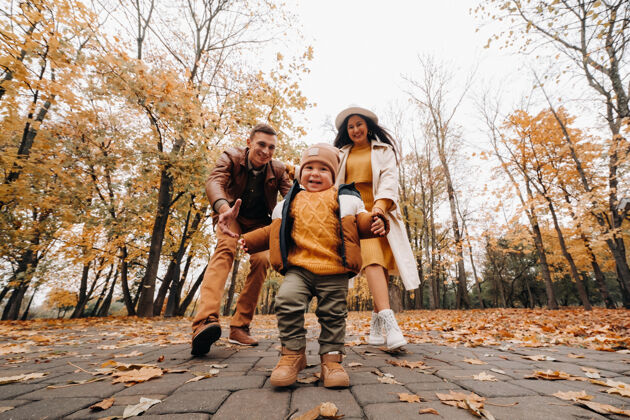 公园爸爸和妈妈带着儿子在秋天的公园里散步一家人在金秋的自然公园里散步乐趣健康母亲