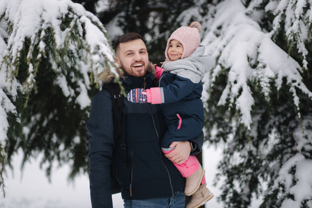 雪可爱的小女儿和她可爱的爸爸站在雪树旁季节小有趣