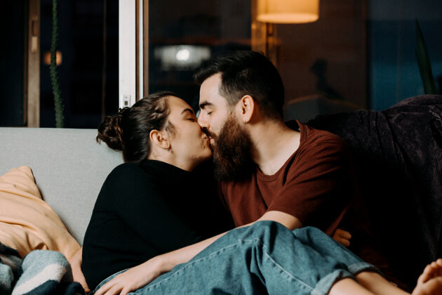 快乐年轻夫妇在沙发上互相亲吻两个人拥抱信任