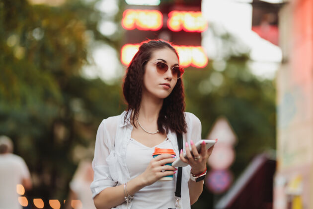 女性一个戴墨镜的女人拿着咖啡走在街上街上高中高质量的照片热饮年轻人选择