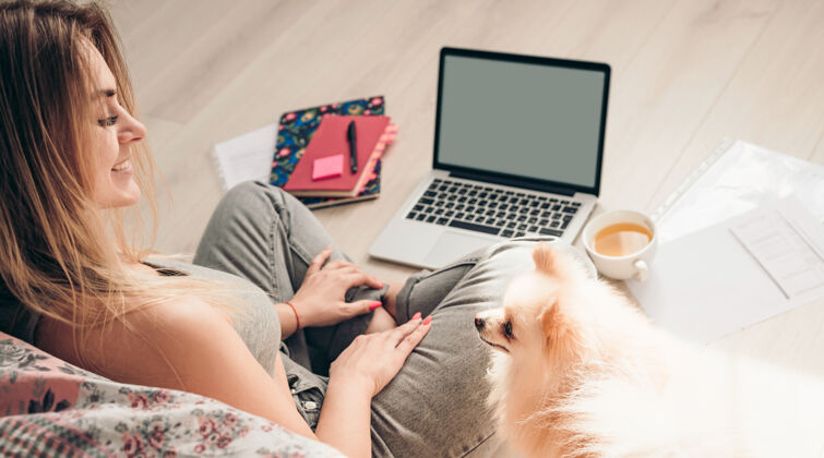 学习一个年轻的女孩和她的狗波美拉尼亚坐在地板上 在一个小农场工作笔记本电脑.狗她在看着她狗女孩学生