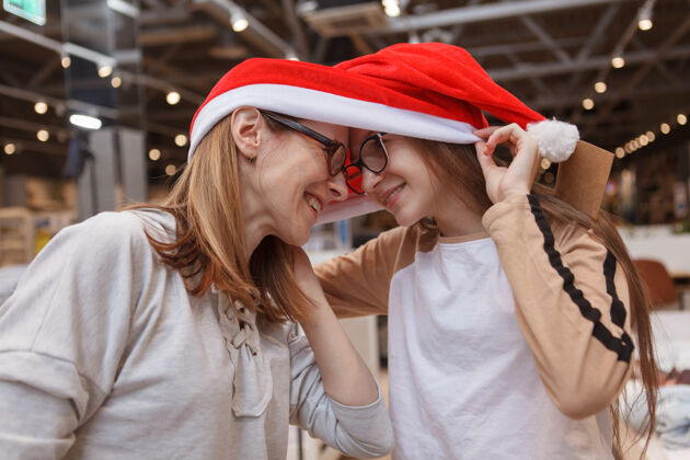 购买少女笑着 和妈妈摸额头 一起戴着圣诞老人的帽子孩子圣诞老人庆祝