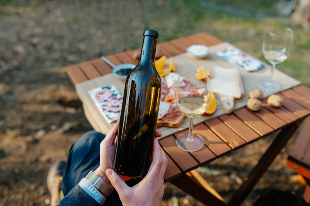 酒杯闭上一只不可辨认的手 手里拿着一瓶酒酒桌提供开胃菜和美味的食物 品酒和野餐的概念放松微笑杯子