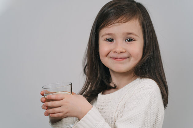 小孩子喝玻璃杯里的水一个黑发女孩拿着一杯水饮料杯子快乐
