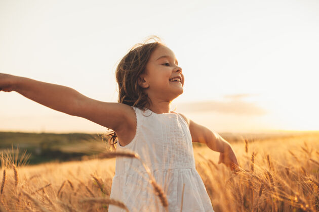 表达美丽的小女孩在麦田里笑着 手举着跑着日落自由概念季节生长天空