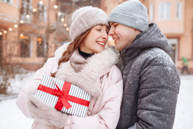 丝带一对幸福的情侣在冬天的雪景公园外 手里拿着红丝带的礼物手高兴男人和女人庆祝情人节一起日期在外面寒冷的冬日手快乐爱