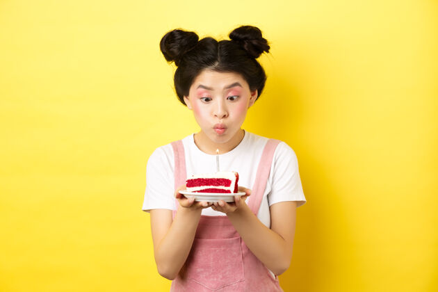 女人节假日庆祝傻亚洲女孩 化着迷人的妆 许愿 在生日蛋糕上吹蜡烛 站在黄色的舞台上蛋糕真实提供