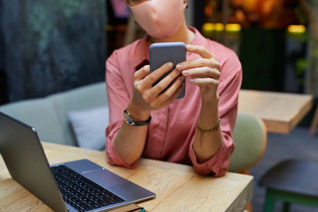 商务大流行期间 戴着口罩的年轻女子在咖啡馆工作时用手机输入信息的特写镜头人手全球通信打字