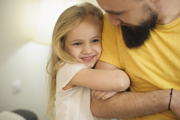 爸爸笑容满面的女孩从床上抱着她的父亲手臂父亲和女儿一起在家度过快乐时光室内父亲金发