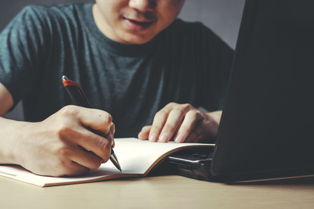 想象年轻的亚裔男子正在家里的书桌旁写作业本白种人小企业笔记