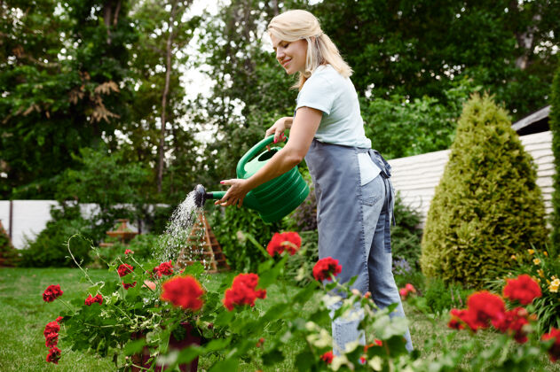 工作围裙里的女人在花园里浇花花园女园丁照顾户外植物 园艺爱好 花匠的生活方式浇水工人花
