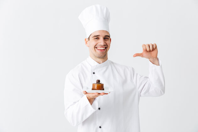 烹饪开朗的厨师穿着制服 在白色的墙上展示一个盘子上的糕点甜点酋长面包师