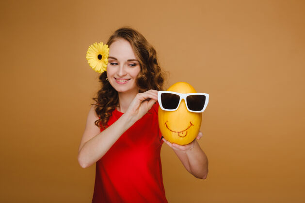 年轻一个快乐的年轻女子拿着一个甜瓜的肖像眼镜.甜瓜一个微笑白色红色连衣裙黄色