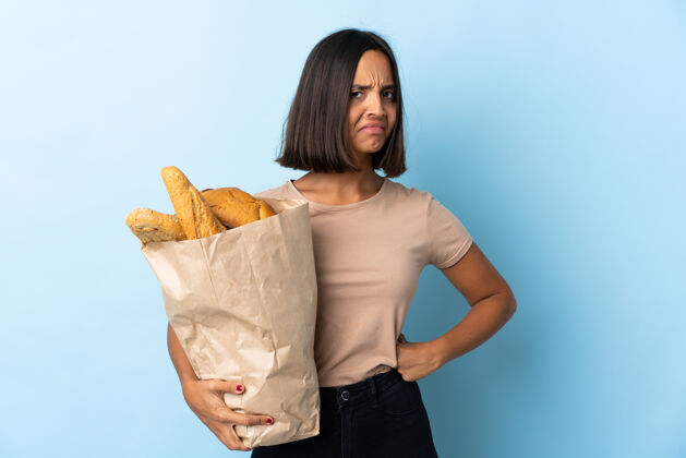 碳水化合物年轻的拉丁女人买了一些面包孤立在蓝色愤怒愤怒失望年轻