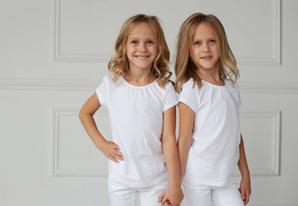 时尚两个穿着白色衣服的双胞胎姐妹手牵手小工作室白布