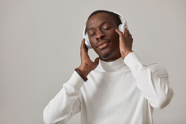 科技戴着耳机的年轻人在灰色的墙上闭着眼睛欣赏着音乐灰色背景欢呼面部表情