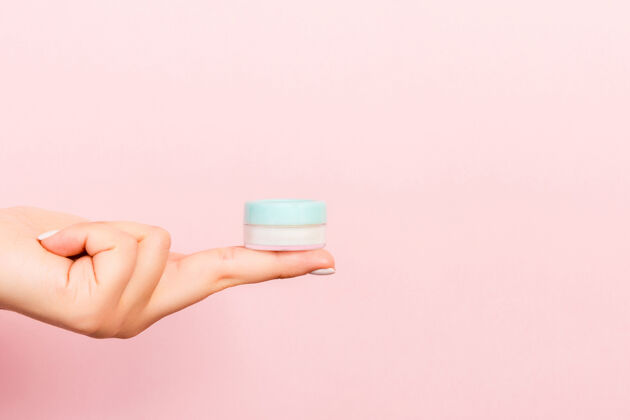 精华女性手拿粉红色背景的化妆品罐的特写镜头乳液水疗卫生