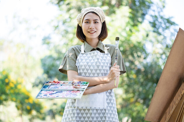 作坊夏日田野里的亚洲美女 用画笔和彩色颜料在花园里的纸艺板上画画调色板快乐休闲