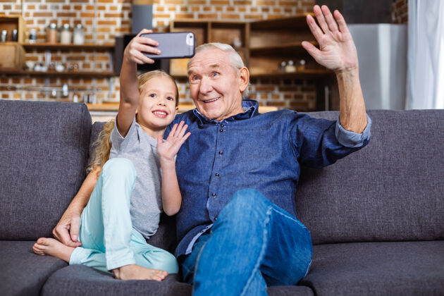 老人快乐微笑的小女孩坐在沙发上和爷爷一起自拍父亲自拍老年人
