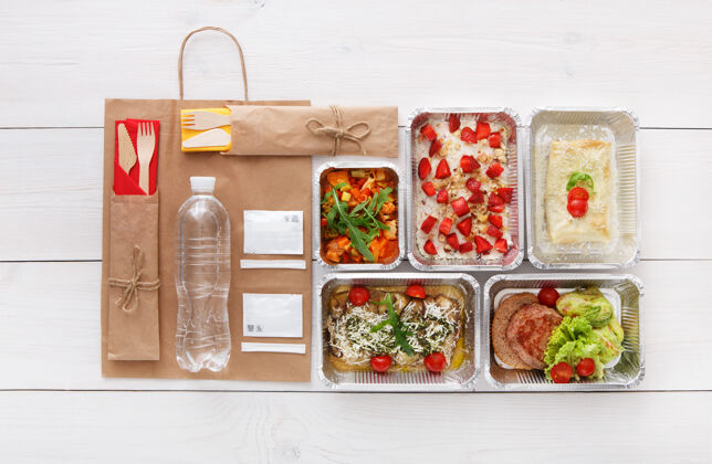 餐食健康食品配送 日常膳食和零食营养 蔬菜 肉类 水瓶和水果在铝箔盒和牛皮纸包装俯视图 平躺在白色的木头盒子外卖蔬菜