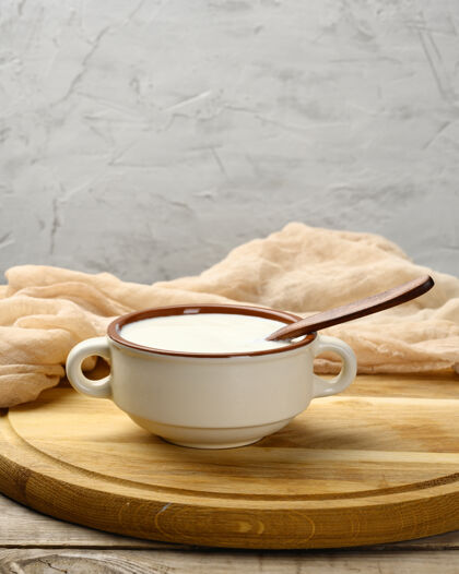 碗酸奶油放在一个棕色的陶瓷碗里 用木勺放在桌子上 是发酵牛奶的有用产品产品健康鞭子